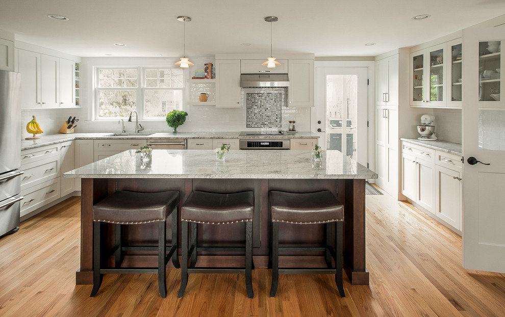 Inspiration for a mid-sized transitional u-shaped kitchen in Boston with an undermount sink, shaker cabinets, white cabinets, white splashback, subway tile splashback, stainless steel appliances, medium hardwood floors, with island and brown floor.