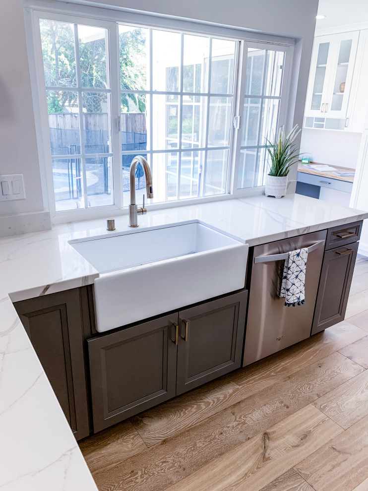 Mid-sized contemporary u-shaped kitchen in San Francisco with a farmhouse sink, shaker cabinets, white cabinets, quartz benchtops, white splashback, marble splashback, stainless steel appliances, light hardwood floors, a peninsula, beige floor and white benchtop.