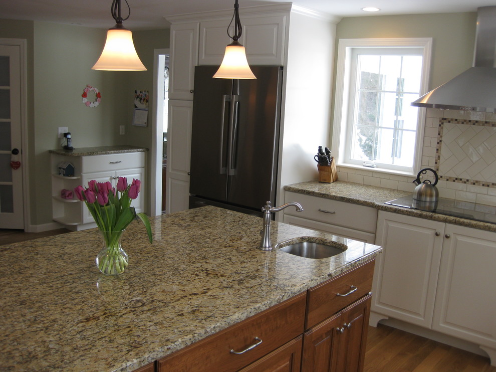 Transitional u-shaped medium tone wood floor eat-in kitchen photo in Boston with an undermount sink, raised-panel cabinets, white cabinets, granite countertops, white backsplash, ceramic backsplash, stainless steel appliances, an island and beige countertops
