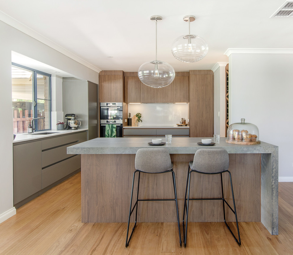 Photo of a contemporary l-shaped kitchen in Perth with an undermount sink, flat-panel cabinets, medium wood cabinets, stainless steel appliances, medium hardwood floors, with island, brown floor and grey benchtop.