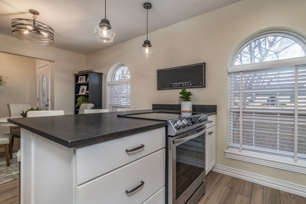 Transitional galley vinyl floor and beige floor eat-in kitchen photo with a double-bowl sink, recessed-panel cabinets, white cabinets, granite countertops, beige backsplash, travertine backsplash, stainless steel appliances, a peninsula and black countertops