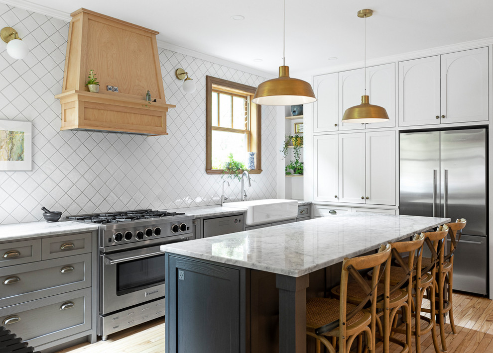 Kitchen - transitional light wood floor kitchen idea with a farmhouse sink, shaker cabinets, gray cabinets, white backsplash, stainless steel appliances, an island and white countertops