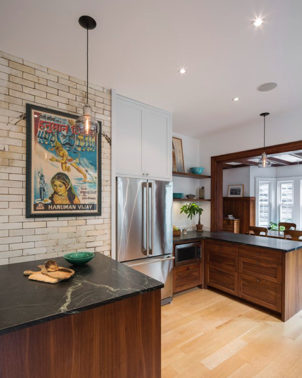 Photo of a mid-sized industrial l-shaped open plan kitchen in New York with an undermount sink, shaker cabinets, dark wood cabinets, soapstone benchtops, white splashback, stone slab splashback, stainless steel appliances, light hardwood floors, a peninsula and beige floor.