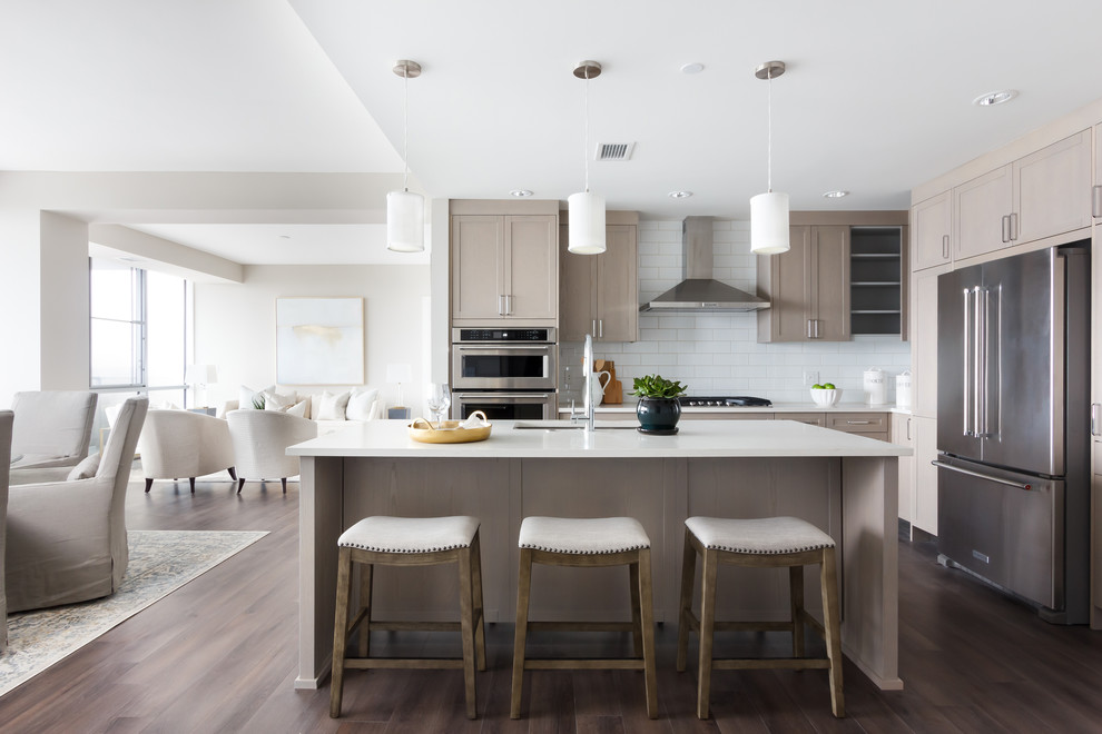Transitional l-shaped open plan kitchen in Other with an undermount sink, shaker cabinets, beige cabinets, white splashback, subway tile splashback, stainless steel appliances, dark hardwood floors, with island, brown floor and white benchtop.