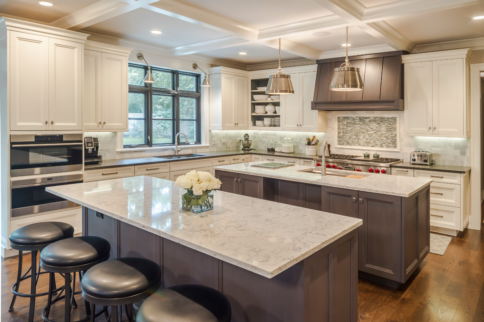 This is an example of an expansive traditional l-shaped kitchen in Chicago with an undermount sink, quartz benchtops, stainless steel appliances, dark hardwood floors, multiple islands, brown floor, recessed-panel cabinets, white cabinets, multi-coloured splashback and mosaic tile splashback.