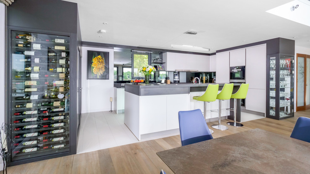 Photo of a large contemporary l-shaped open plan kitchen in Gloucestershire with an integrated sink, flat-panel cabinets, white cabinets, quartzite benchtops, grey splashback, glass sheet splashback, black appliances, with island and black benchtop.