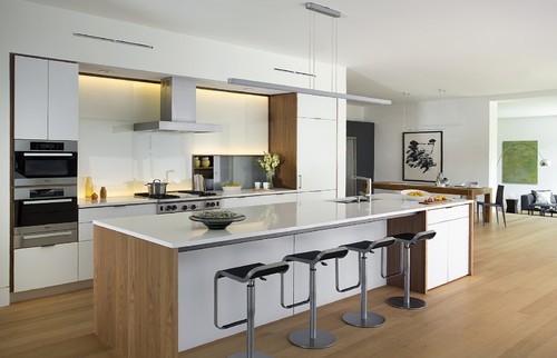 Modern open-plan kitchen with flat-panel RTA cabinets, wood accents, long waterfall island with four stools, integrated appliances, and linear pendants.