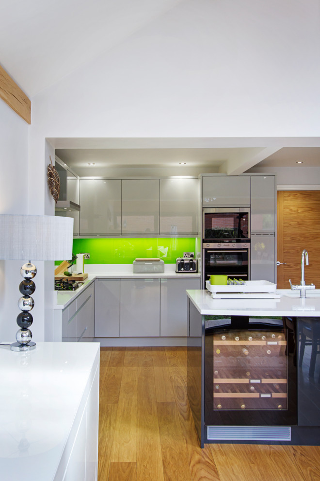 This is an example of a small contemporary l-shaped open plan kitchen in West Midlands with a drop-in sink, flat-panel cabinets, grey cabinets, granite benchtops, green splashback, glass sheet splashback, stainless steel appliances, laminate floors, with island, beige floor, white benchtop and vaulted.