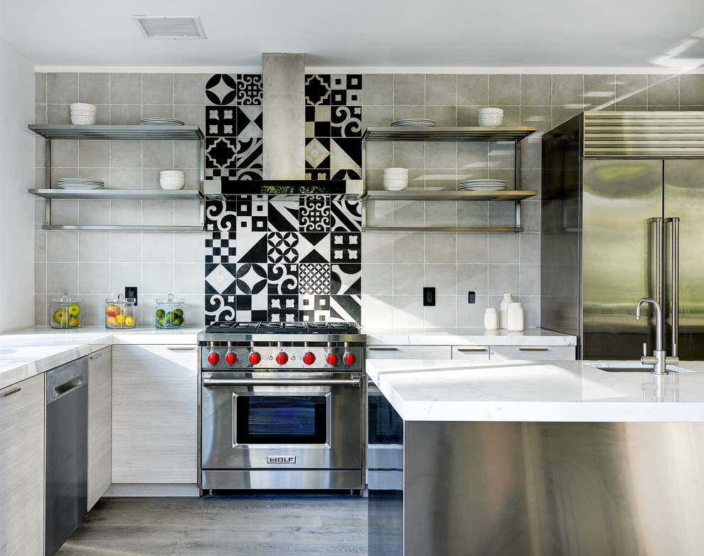 This is an example of a mid-sized contemporary l-shaped open plan kitchen in Los Angeles with an undermount sink, recessed-panel cabinets, grey cabinets, grey splashback, stainless steel appliances, light hardwood floors, with island, grey floor, marble benchtops and cement tile splashback.