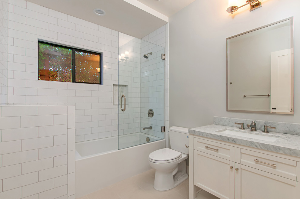 Mid-sized arts and crafts kids bathroom in San Diego with beaded inset cabinets, white cabinets, marble benchtops, an alcove tub, a shower/bathtub combo, a two-piece toilet, white tile, subway tile, grey walls, an undermount sink, beige floor and grey benchtops.