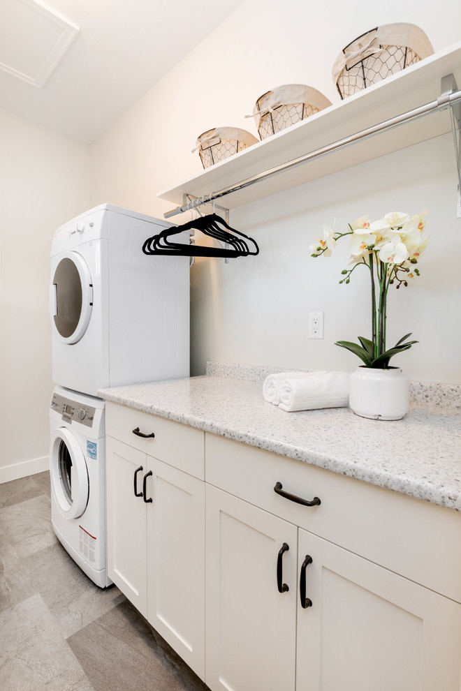 Design ideas for a small transitional single-wall dedicated laundry room in Other with shaker cabinets, white cabinets, grey walls, vinyl floors, a stacked washer and dryer, limestone benchtops and beige floor.