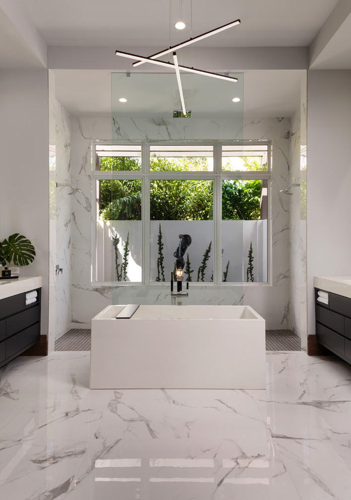 Photo of a large modern master bathroom in Miami with flat-panel cabinets, black cabinets, a freestanding tub, a curbless shower, grey walls, marble floors, an undermount sink, engineered quartz benchtops, white floor, a hinged shower door and white benchtops.