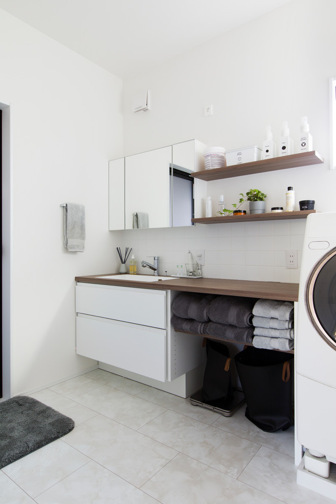 Single-wall dedicated laundry room in Nagoya with a drop-in sink, flat-panel cabinets, white cabinets, wood benchtops, white walls, beige floor and brown benchtop.