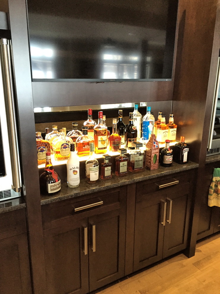 Design ideas for a mid-sized traditional home bar in Ottawa with shaker cabinets, brown cabinets, granite benchtops, mirror splashback and light hardwood floors.