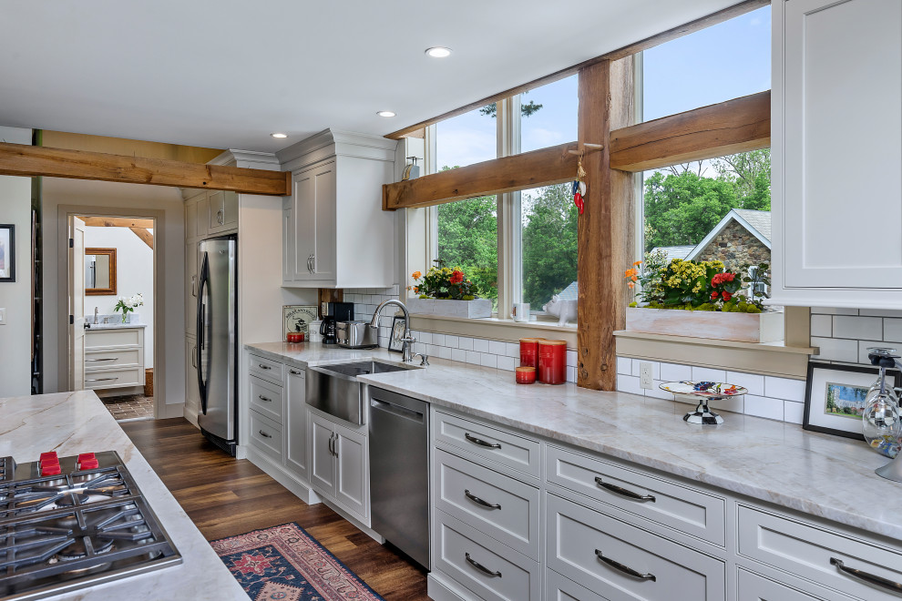 Foto på ett mellanstort lantligt vit kök, med en rustik diskho, skåp i shakerstil, blå skåp, bänkskiva i kvarts, vitt stänkskydd, stänkskydd i porslinskakel, rostfria vitvaror, mellanmörkt trägolv, en köksö och brunt golv