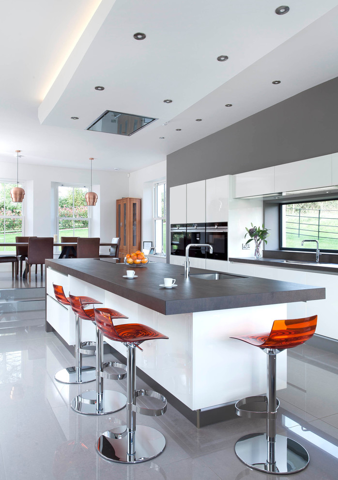 Large contemporary single-wall open plan kitchen in Belfast with an integrated sink, flat-panel cabinets, white cabinets, quartz benchtops, grey splashback, stone slab splashback, stainless steel appliances, porcelain floors and with island.
