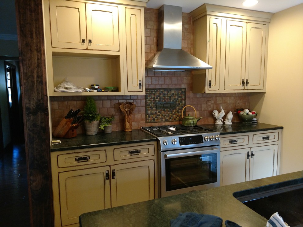 Inspiration for a small rustic kitchen remodel with a single-bowl sink, recessed-panel cabinets, distressed cabinets, granite countertops, multicolored backsplash, ceramic backsplash, stainless steel appliances and an island