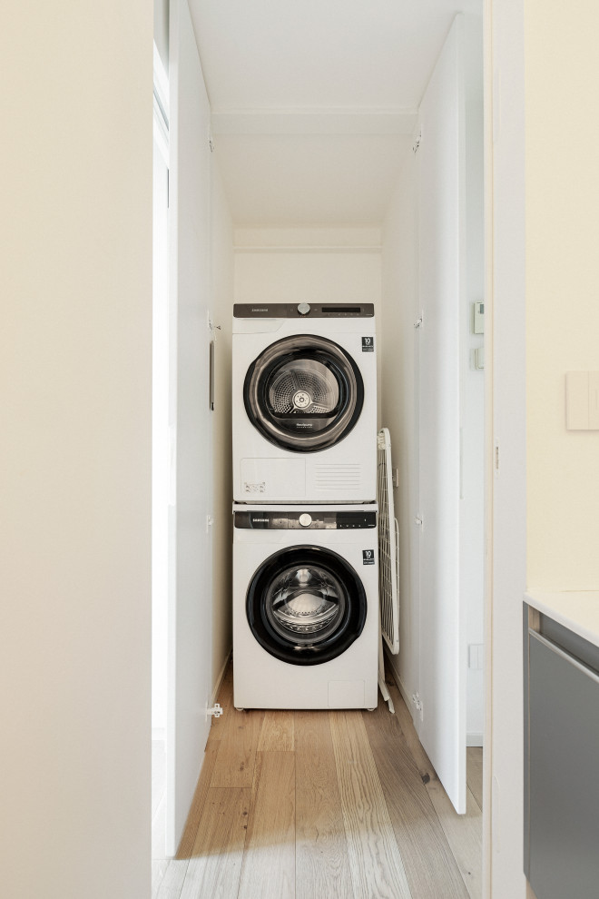 Foto på en liten skandinavisk linjär tvättstuga enbart för tvätt, med släta luckor, vita väggar, ljust trägolv och en tvättpelare