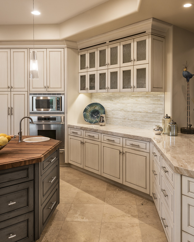 Photo of a mid-sized transitional open plan kitchen in Phoenix with a farmhouse sink, glass-front cabinets, beige cabinets, quartzite benchtops, white splashback, glass tile splashback, stainless steel appliances, travertine floors, with island and beige floor.
