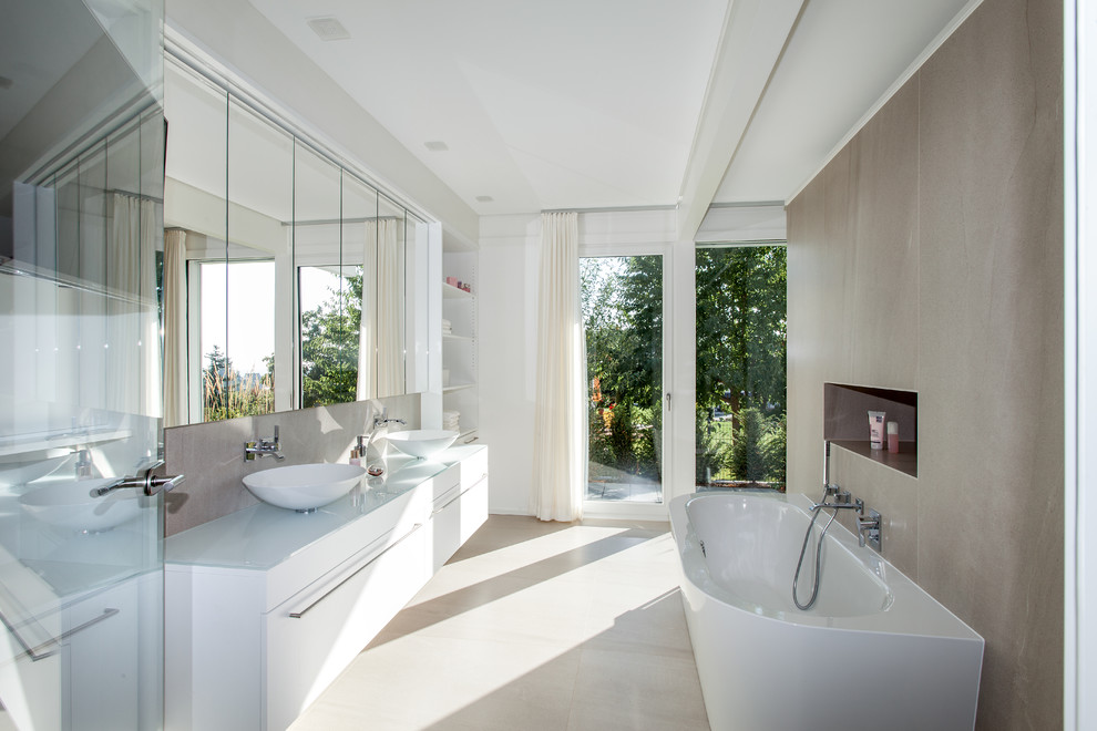 Mid-sized contemporary 3/4 bathroom in Other with flat-panel cabinets, white cabinets, a freestanding tub, beige tile, cement tile, white walls, cement tiles, a vessel sink, glass benchtops and beige floor.