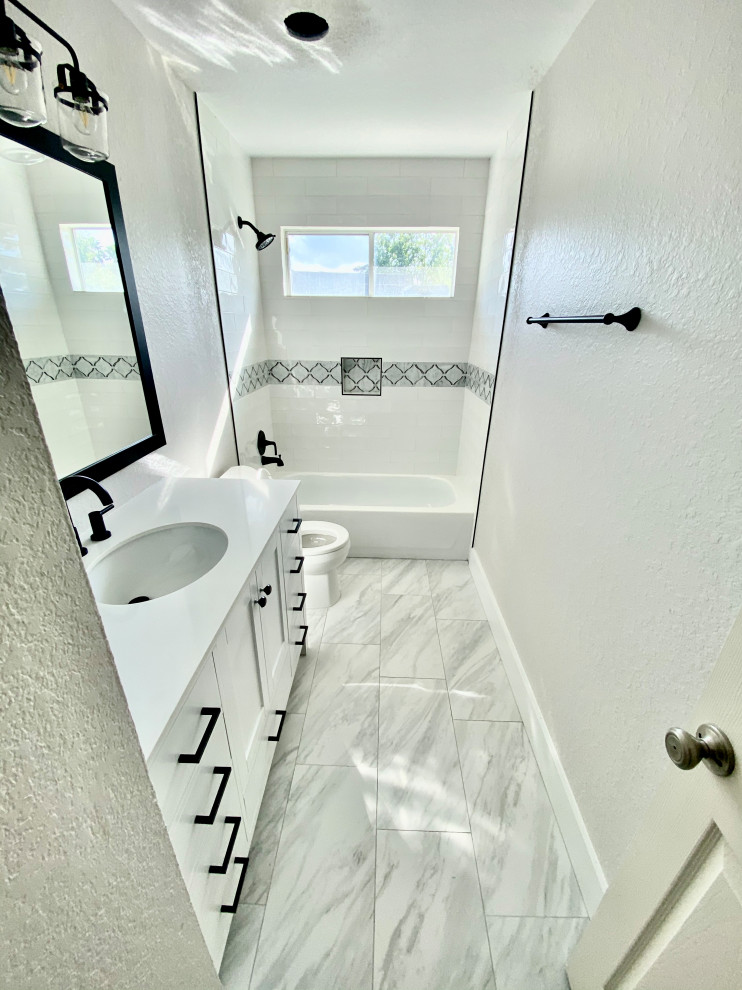 Mid-sized contemporary kids bathroom in Houston with furniture-like cabinets, white cabinets, a drop-in tub, a shower/bathtub combo, a one-piece toilet, multi-coloured tile, glass tile, white walls, porcelain floors, an integrated sink, engineered quartz benchtops, grey floor and white benchtops.