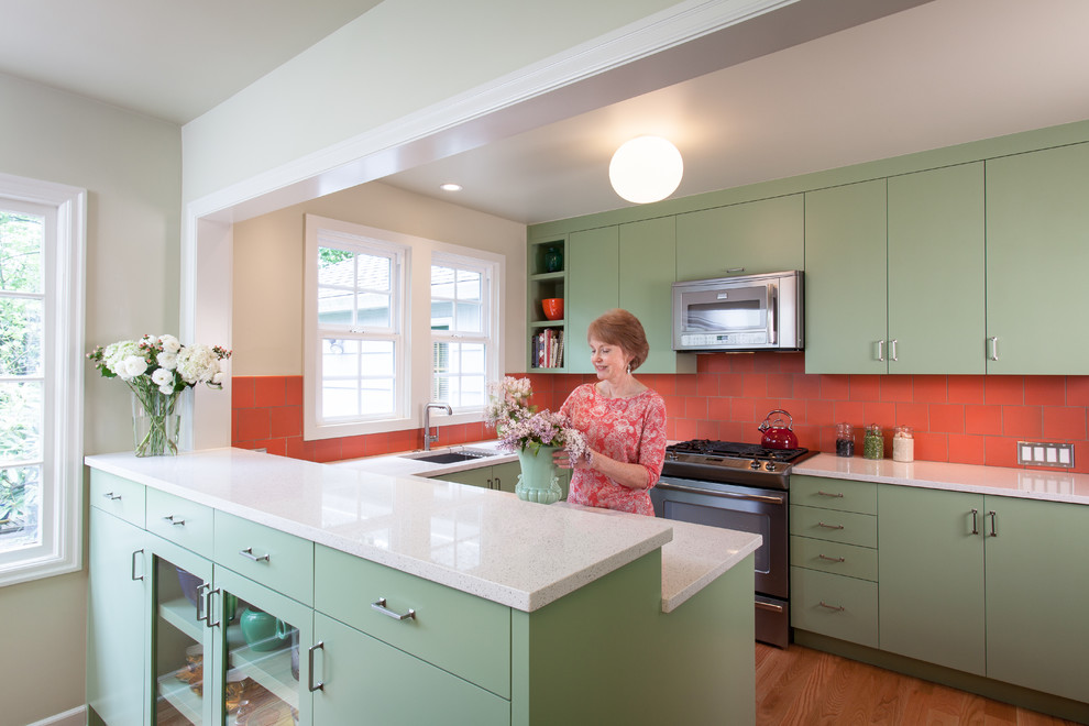 Photo of a small transitional u-shaped eat-in kitchen in Portland with an undermount sink, flat-panel cabinets, green cabinets, recycled glass benchtops, orange splashback, ceramic splashback, stainless steel appliances and light hardwood floors.