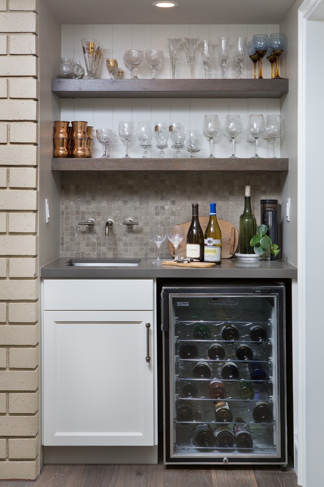 This is an example of a small traditional single-wall wet bar in Orange County with an undermount sink, shaker cabinets, white cabinets, quartz benchtops, grey splashback, stone tile splashback, dark hardwood floors and brown floor.