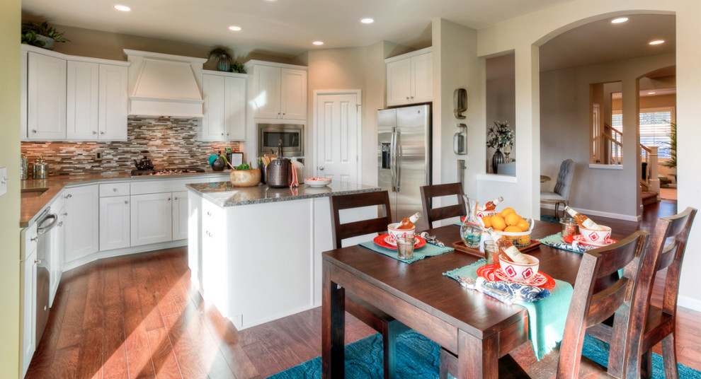 Example of a mid-sized transitional u-shaped medium tone wood floor open concept kitchen design in Seattle with an undermount sink, shaker cabinets, white cabinets, granite countertops, gray backsplash, mosaic tile backsplash, stainless steel appliances and an island