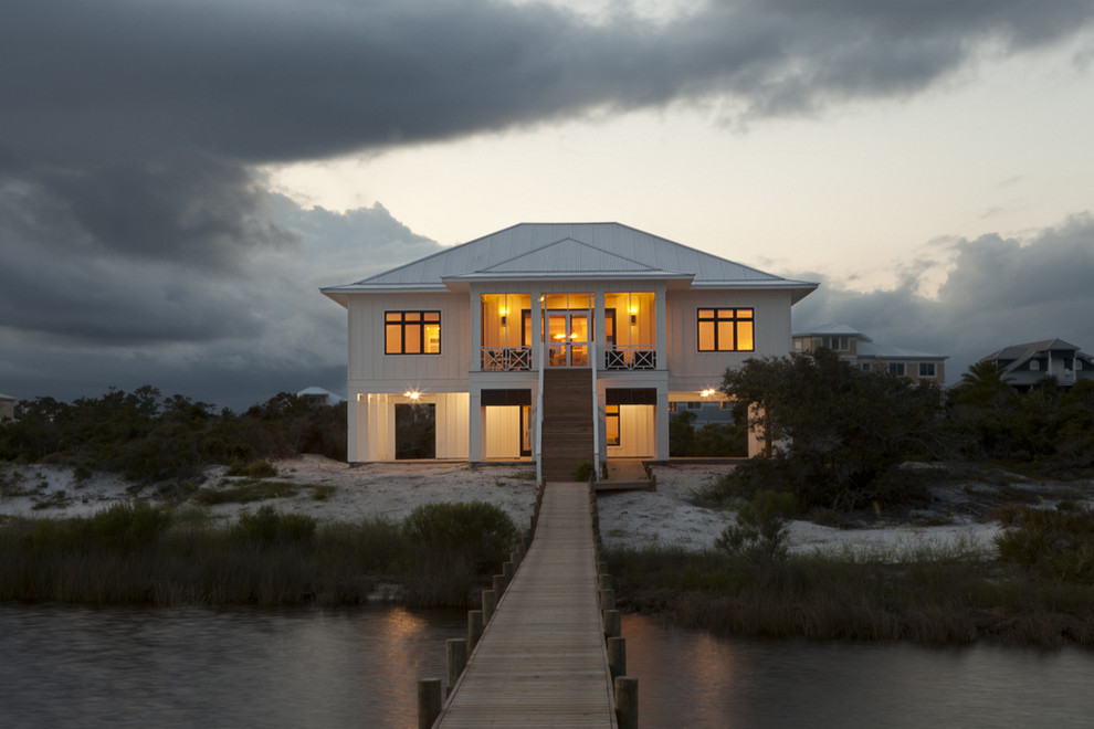 Photo of a large beach style two-storey white house exterior in Miami with a hip roof, wood siding and a metal roof.