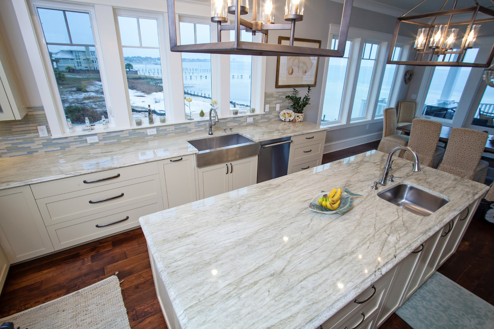 Example of a mid-sized beach style l-shaped medium tone wood floor eat-in kitchen design in Miami with a farmhouse sink, shaker cabinets, white cabinets, quartzite countertops, stainless steel appliances and an island