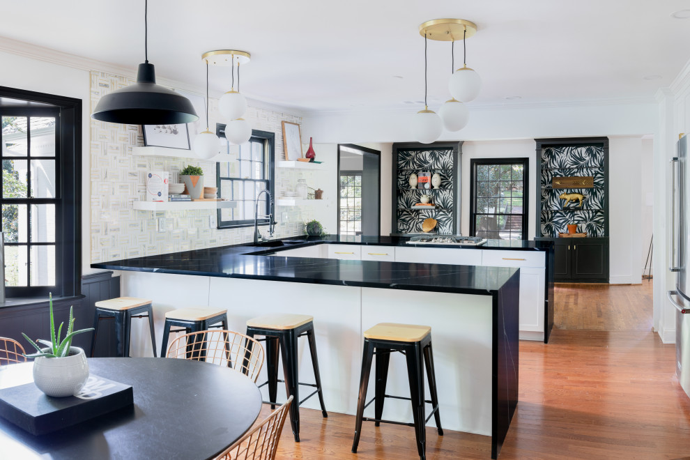 Photo of a transitional u-shaped eat-in kitchen in Other with a single-bowl sink, shaker cabinets, white cabinets, multi-coloured splashback, medium hardwood floors, a peninsula and black benchtop.