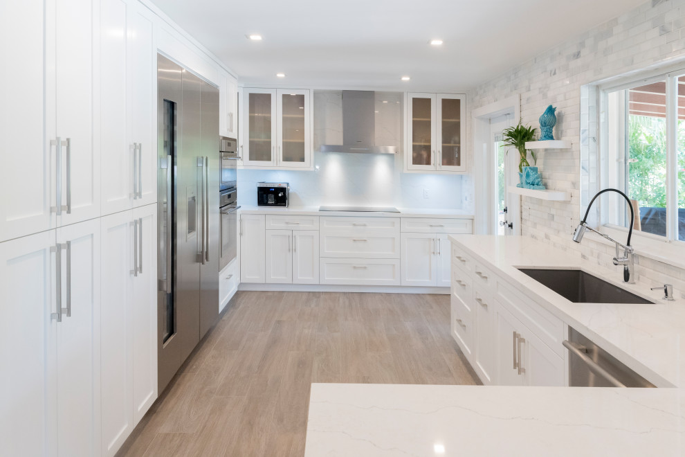Inspiration for a mid-sized transitional galley light wood floor kitchen pantry remodel in Miami with an undermount sink, shaker cabinets, white cabinets, quartz countertops, white backsplash, marble backsplash, stainless steel appliances and white countertops