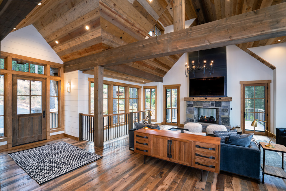 Mid-sized country open concept living room in Other with white walls, medium hardwood floors, a two-sided fireplace, a stone fireplace surround, a wall-mounted tv and brown floor.