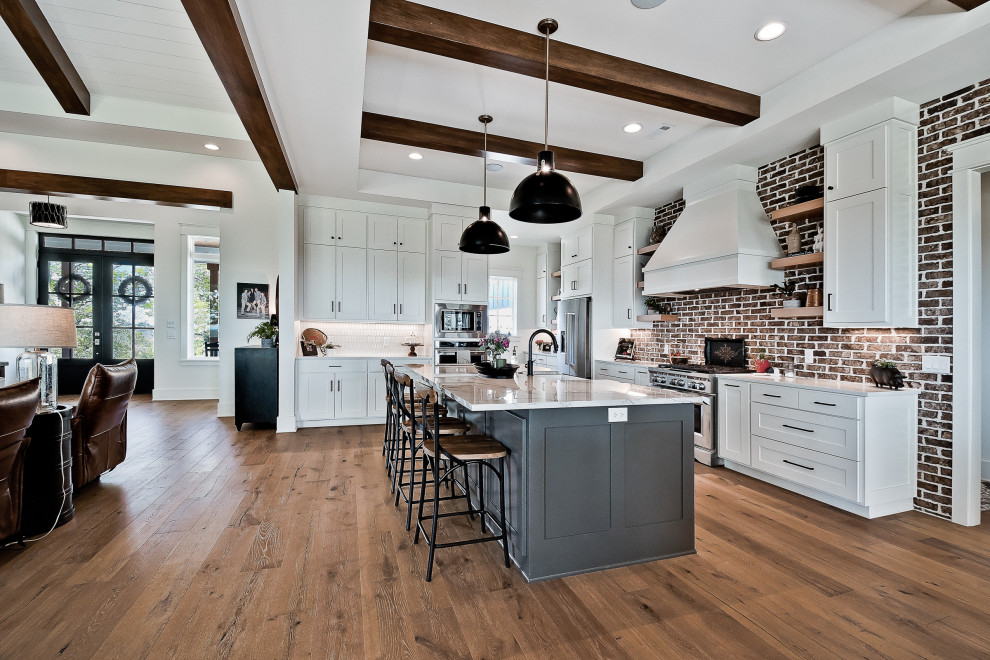 Inspiration for a large country u-shaped eat-in kitchen in Other with a farmhouse sink, raised-panel cabinets, white cabinets, quartz benchtops, red splashback, brick splashback, stainless steel appliances, light hardwood floors, with island, white benchtop and exposed beam.