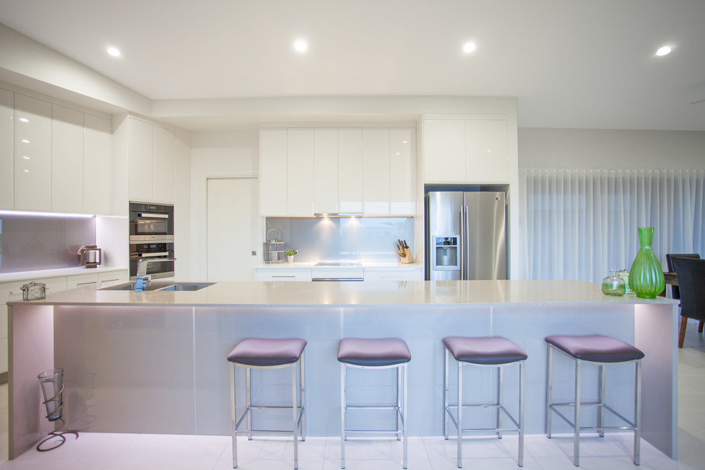 Design ideas for a mid-sized contemporary galley open plan kitchen in Other with granite benchtops, with island, an undermount sink, flat-panel cabinets, white cabinets, grey splashback, ceramic splashback, stainless steel appliances, ceramic floors, white floor and beige benchtop.