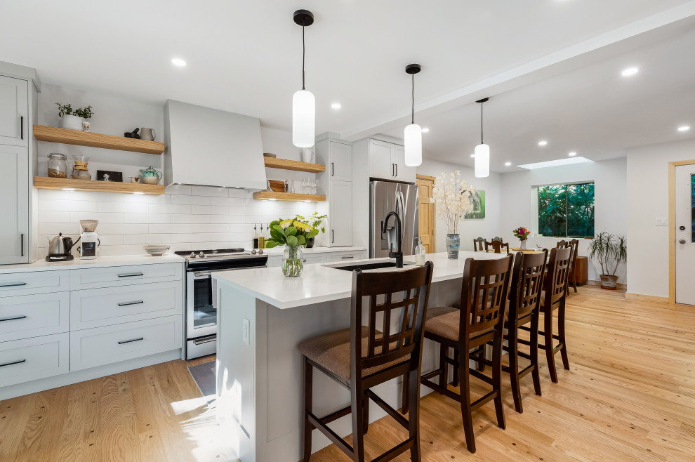 This is an example of a mid-sized scandinavian l-shaped eat-in kitchen in Vancouver with an undermount sink, shaker cabinets, grey cabinets, quartzite benchtops, white splashback, subway tile splashback, stainless steel appliances, medium hardwood floors, with island, brown floor, white benchtop and timber.