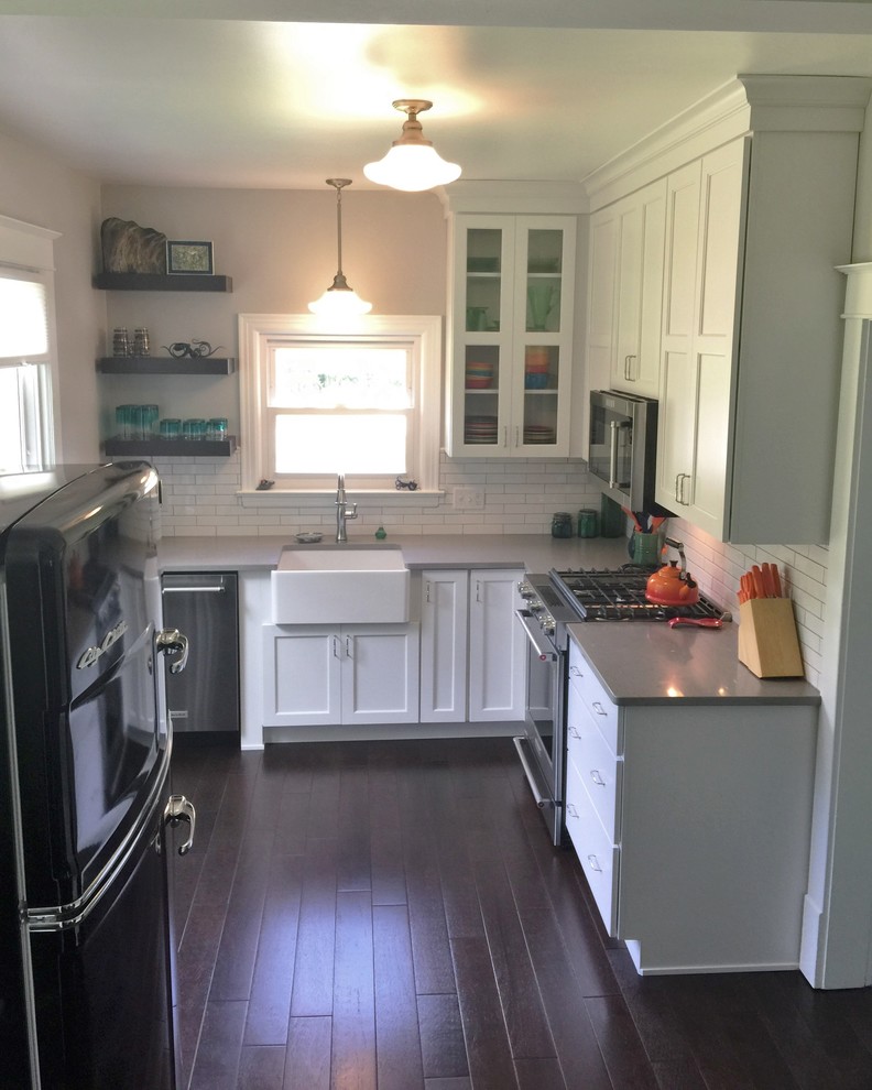 This is an example of a small transitional l-shaped separate kitchen in Chicago with a farmhouse sink, flat-panel cabinets, white cabinets, quartz benchtops, white splashback, subway tile splashback, stainless steel appliances, dark hardwood floors and no island.