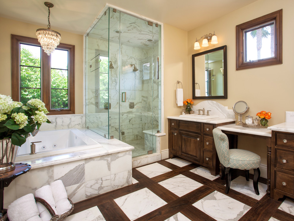 This is an example of a tropical bathroom in San Diego with raised-panel cabinets, dark wood cabinets, marble benchtops, a drop-in tub, a corner shower, white tile and stone tile.