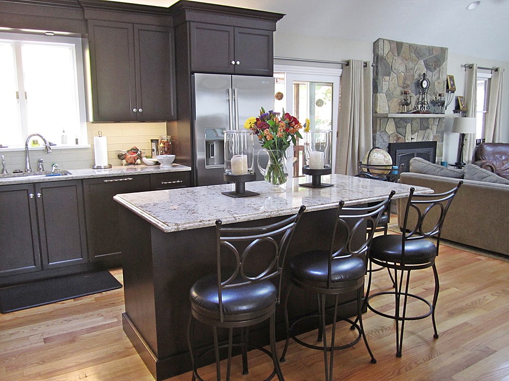 Example of a large transitional l-shaped light wood floor eat-in kitchen design with an undermount sink, shaker cabinets, black cabinets, marble countertops, white backsplash, subway tile backsplash, stainless steel appliances and an island