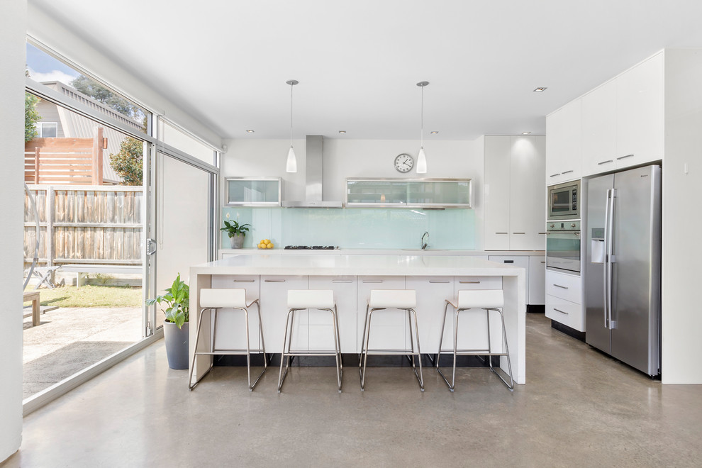 Photo of a contemporary l-shaped kitchen in Melbourne with flat-panel cabinets, white cabinets, stainless steel appliances, concrete floors, with island, grey floor and grey benchtop.