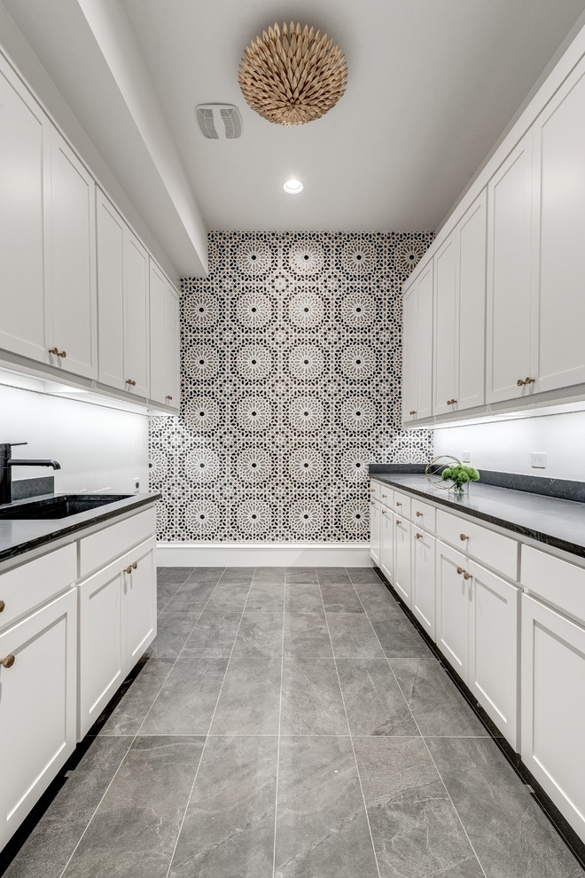 Inspiration for a large mediterranean galley dedicated laundry room in Dallas with an undermount sink, shaker cabinets, white cabinets, granite benchtops, white walls, a side-by-side washer and dryer, black benchtop, porcelain floors and grey floor.