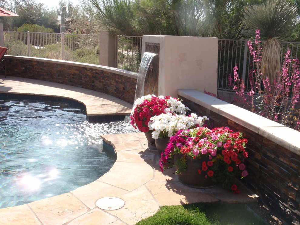 This is an example of a mid-sized contemporary backyard custom-shaped lap pool in Phoenix with a water feature and natural stone pavers.