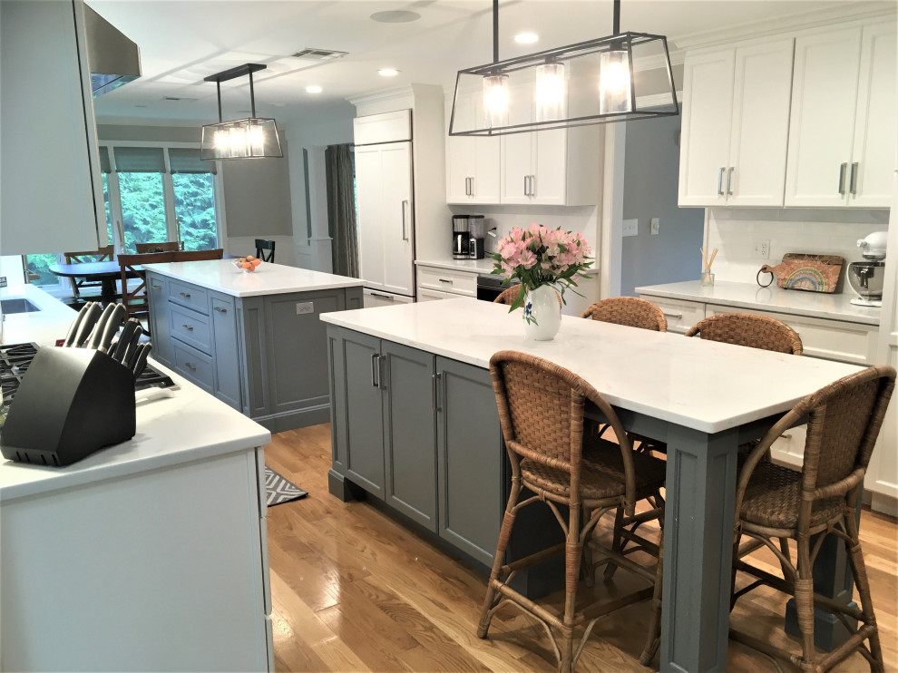 Large transitional galley light wood floor and brown floor eat-in kitchen photo in Boston with an undermount sink, shaker cabinets, white cabinets, quartz countertops, white backsplash, subway tile backsplash, stainless steel appliances, two islands and white countertops