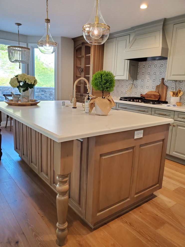 Mid-sized french country l-shaped medium tone wood floor open concept kitchen photo in Orange County with a farmhouse sink, raised-panel cabinets, green cabinets, quartz countertops, white backsplash, marble backsplash, white appliances, an island and white countertops