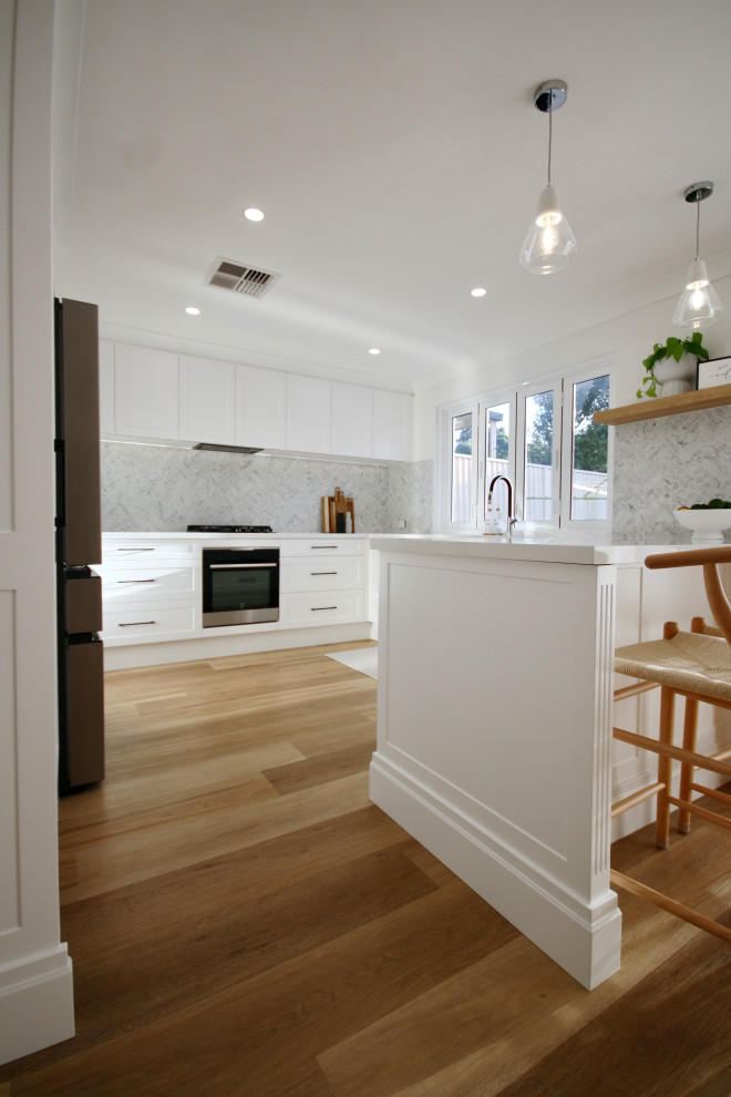 Idéer för att renovera ett mellanstort funkis vit vitt kök, med en undermonterad diskho, skåp i shakerstil, vita skåp, bänkskiva i kvarts, grått stänkskydd, stänkskydd i marmor, svarta vitvaror, mellanmörkt trägolv, en köksö och brunt golv