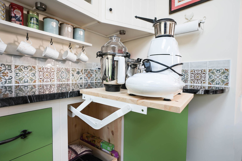 Photo of a small country l-shaped eat-in kitchen in Essex with a farmhouse sink, green cabinets, granite benchtops, multi-coloured splashback, mosaic tile splashback, panelled appliances, porcelain floors, with island, multi-coloured floor and black benchtop.