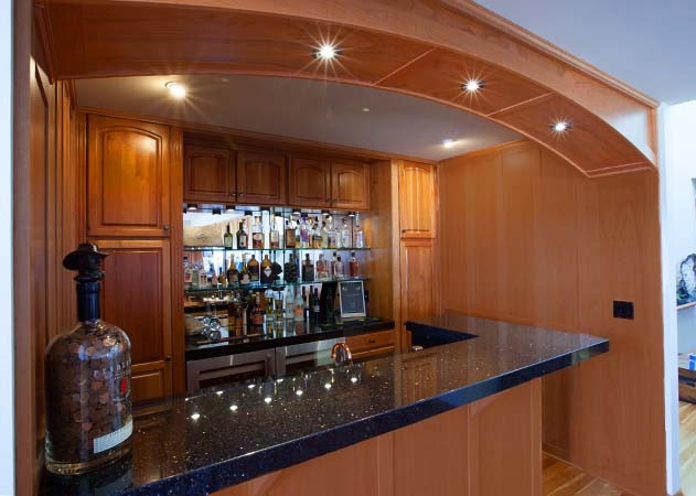 Design ideas for a large arts and crafts single-wall seated home bar in Portland with a drop-in sink, raised-panel cabinets, medium wood cabinets, laminate benchtops, mirror splashback, medium hardwood floors, brown floor and black benchtop.