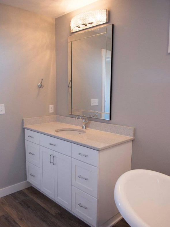 Mid-sized transitional master medium tone wood floor and brown floor freestanding bathtub photo with recessed-panel cabinets, white cabinets, a one-piece toilet, gray walls, an undermount sink, granite countertops and gray countertops