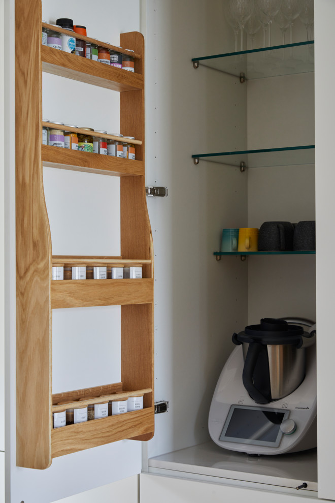 Modern inredning av ett mellanstort vit linjärt vitt kök och matrum, med en undermonterad diskho, släta luckor, vita skåp, bänkskiva i kvarts, vitt stänkskydd, svarta vitvaror, mellanmörkt trägolv och brunt golv