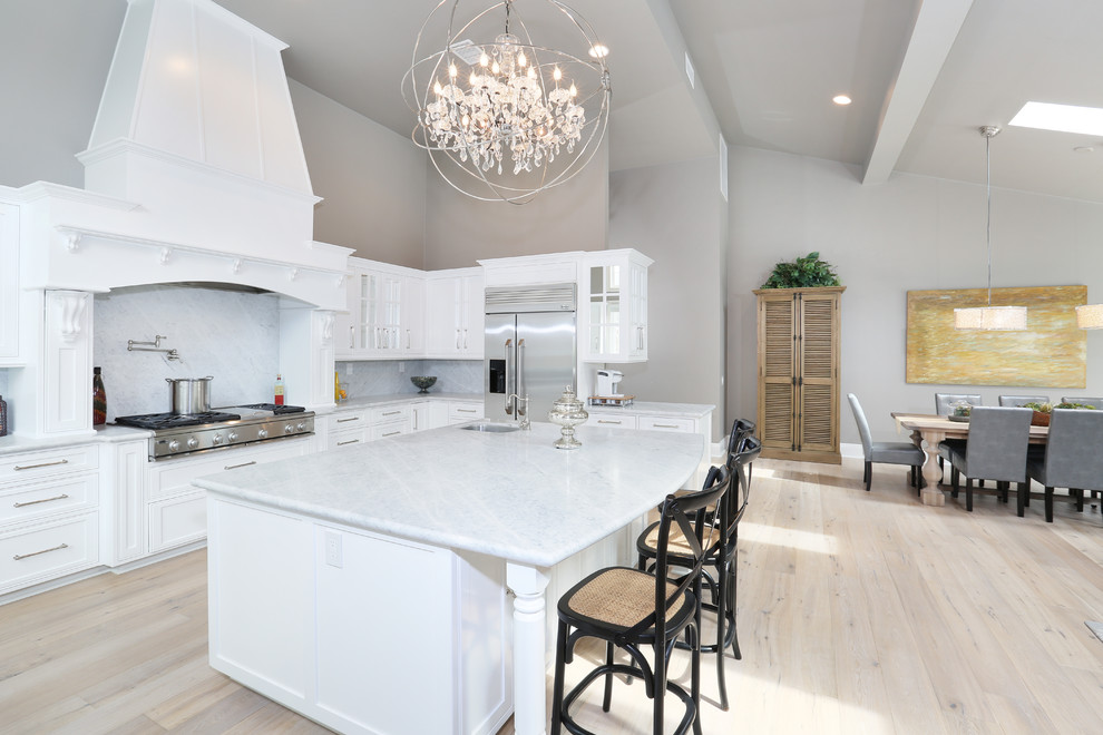 Design ideas for a traditional l-shaped eat-in kitchen in Orange County with an undermount sink, recessed-panel cabinets, white cabinets, white splashback, stainless steel appliances, light hardwood floors and with island.